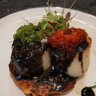 Vieiras sobre careta de cerdo, jugo de tinta, tobiko y tobiko con wasabi